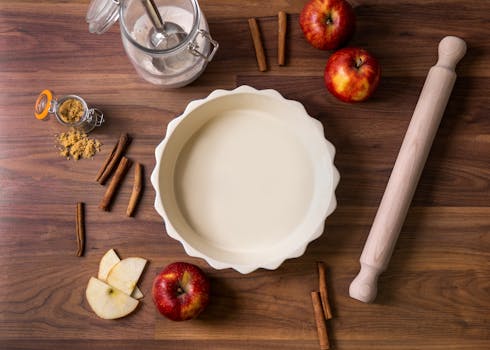 Ingrédients pour une tarte aux pommes : pâte à tarte, pommes, cannelle, sucre et rouleau à pâtisserie sur une table en bois.