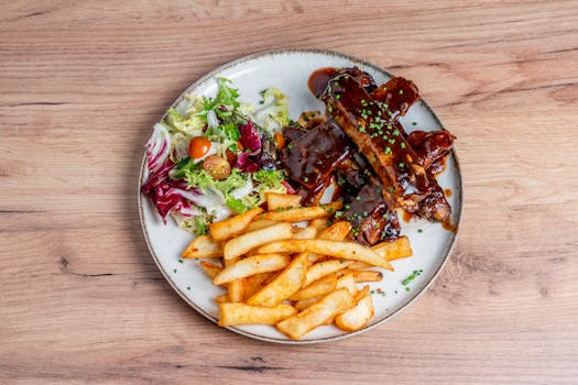 Assiette de travers de porc caramélisés avec sauce BBQ, accompagnés de frites dorées et d'une salade fraîche.