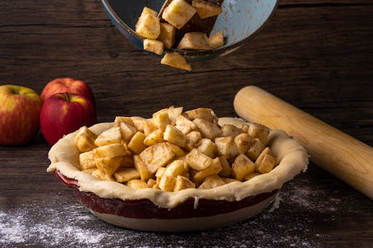 Pommes coupées en dés versées dans une croûte de tarte, avec des pommes entières et un rouleau à pâtisserie en arrière-plan.