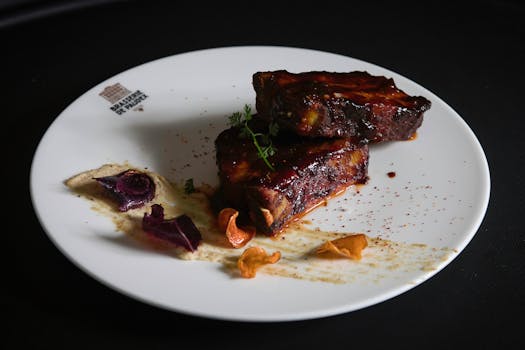Travers de porc caramélisés au barbecue, présentés sur une assiette avec garniture colorée.