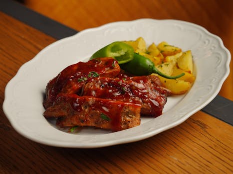 Travers de porc au four nappés de sauce BBQ caramélisée, accompagnés de pommes de terre et piments verts.