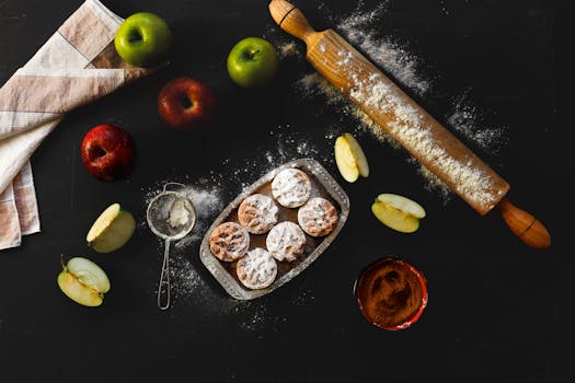 Ingrédients pour tarte aux pommes : pommes vertes et rouges, pâte, rouleau à pâtisserie, sucre et épices sur une table noire.